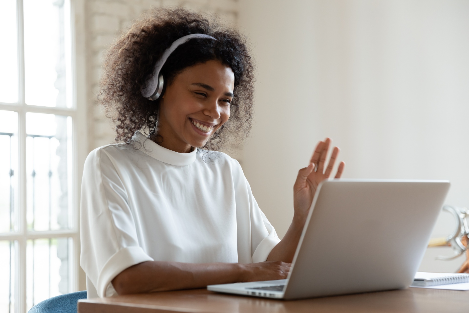 Woman on a video call waving at her laptop